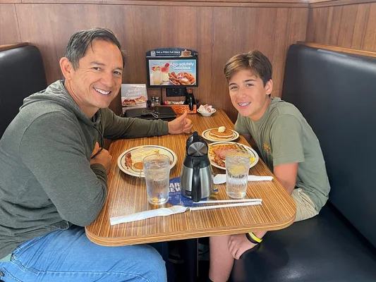 DR. Taylor and his sone eating breakfast at an Ihop. Both are smiling and Dr. Taylor is giving a thumbs up