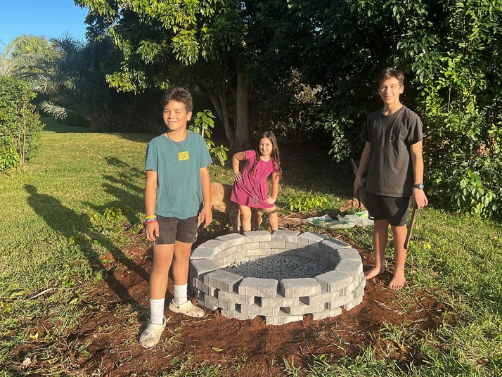 3 kids standing around a firepit.