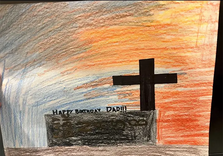 Child’s drawing of a cross at sunset with a birthday message on a stone-like structure.