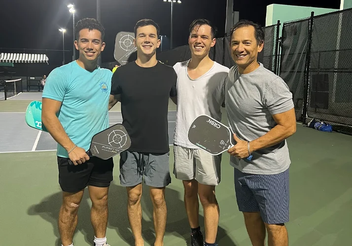 Dr.Derek Taylor with friends standing on a lit court holding pickleball paddles after a match.